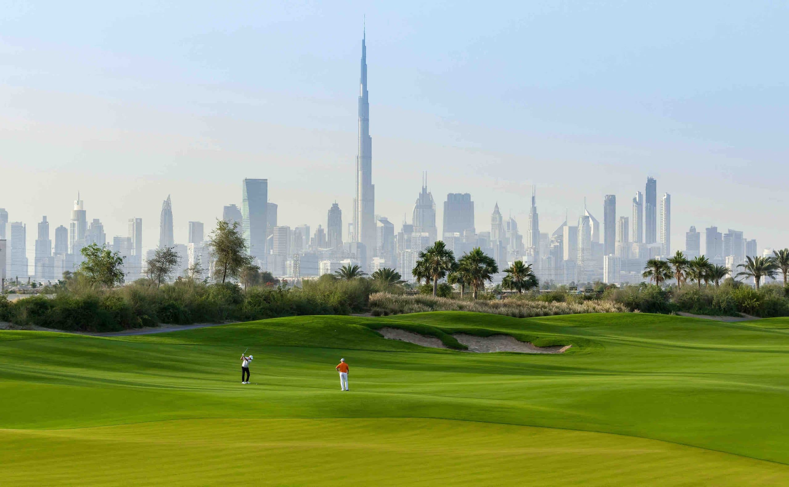 Green fairways and trees in front of the Dubai skyline