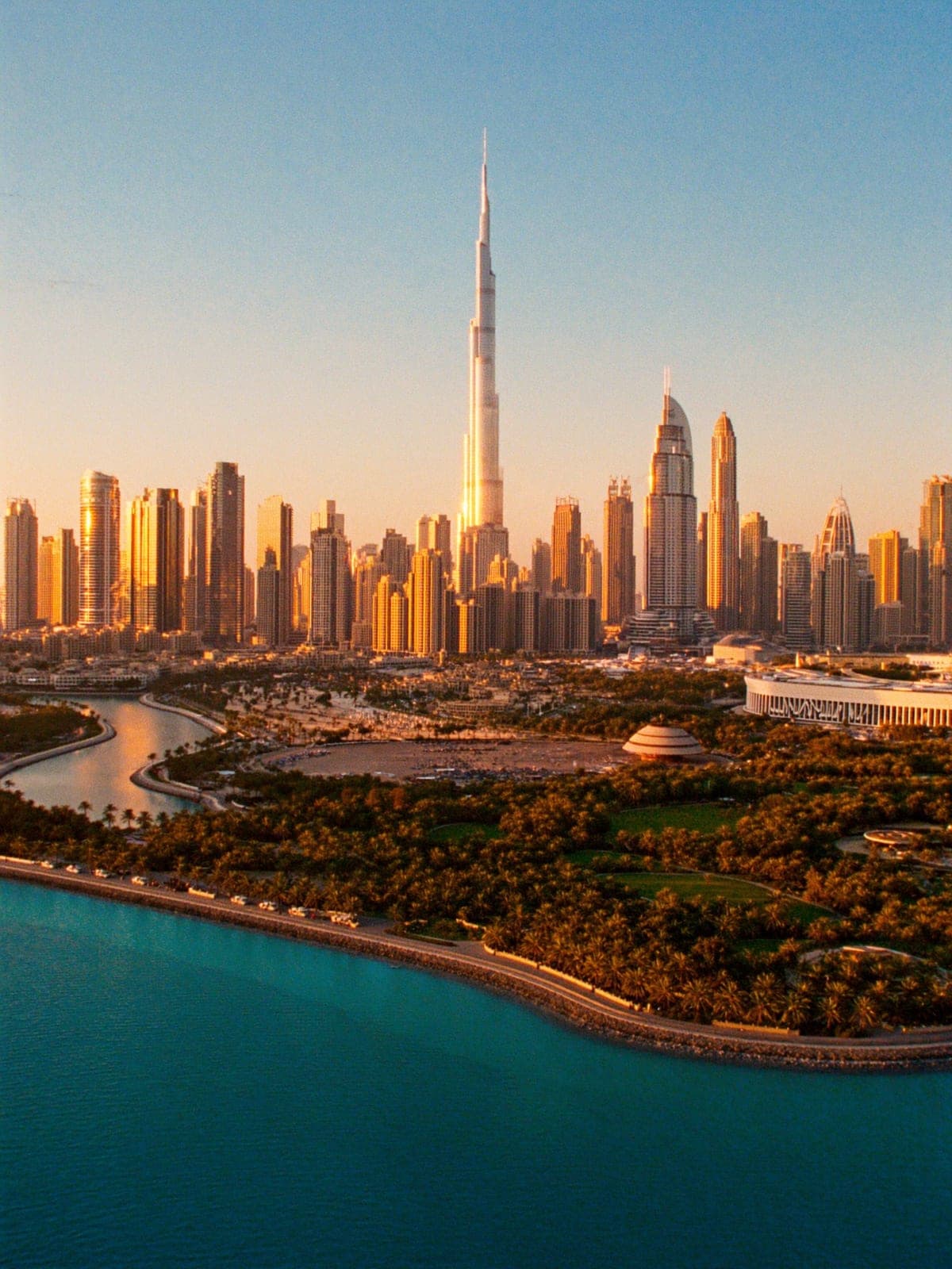 Downtown Dubai and the Burj Khalifa above a park and the sea at sunset